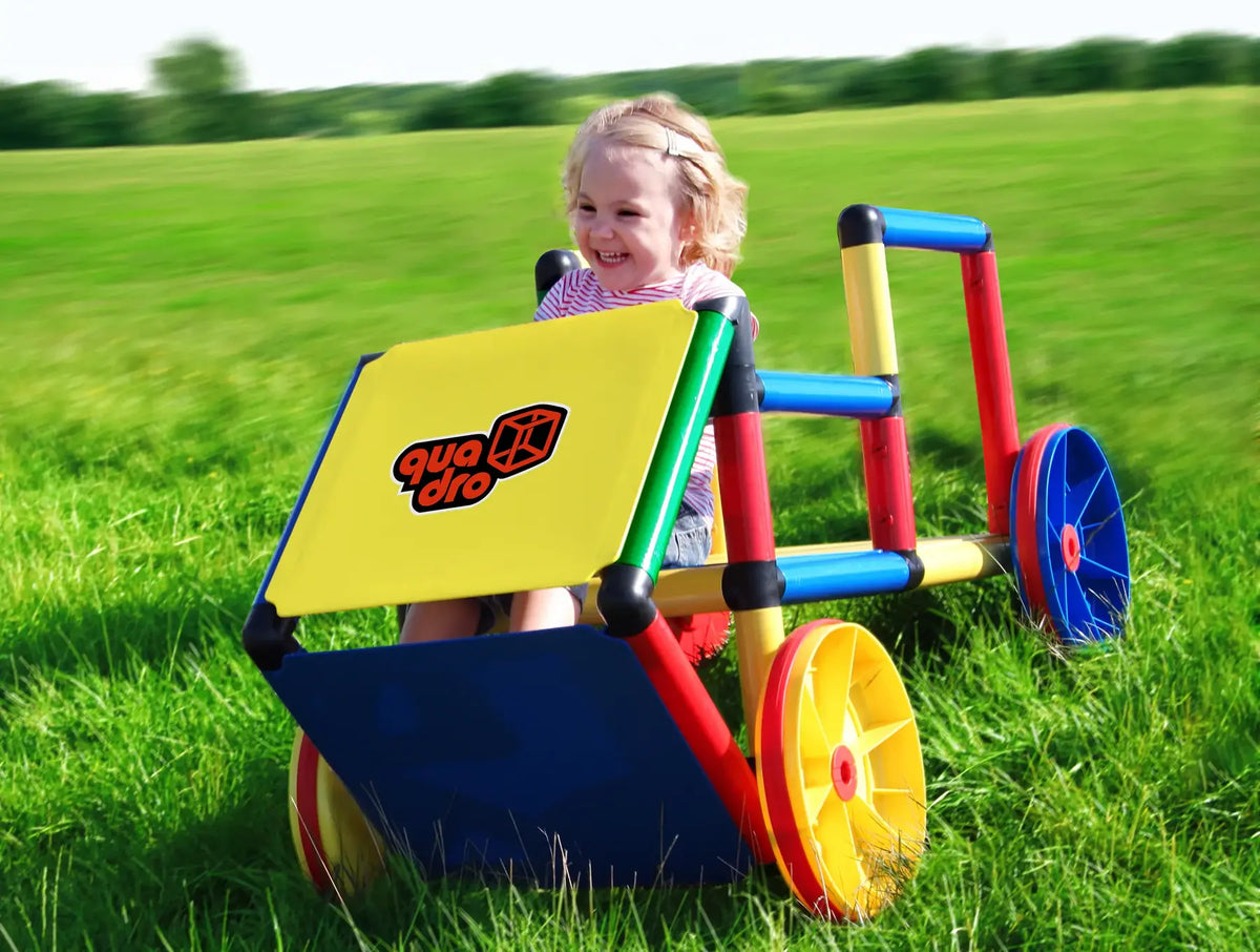 Child pushing a colourful QUADRO wheeled cart across a grassy field