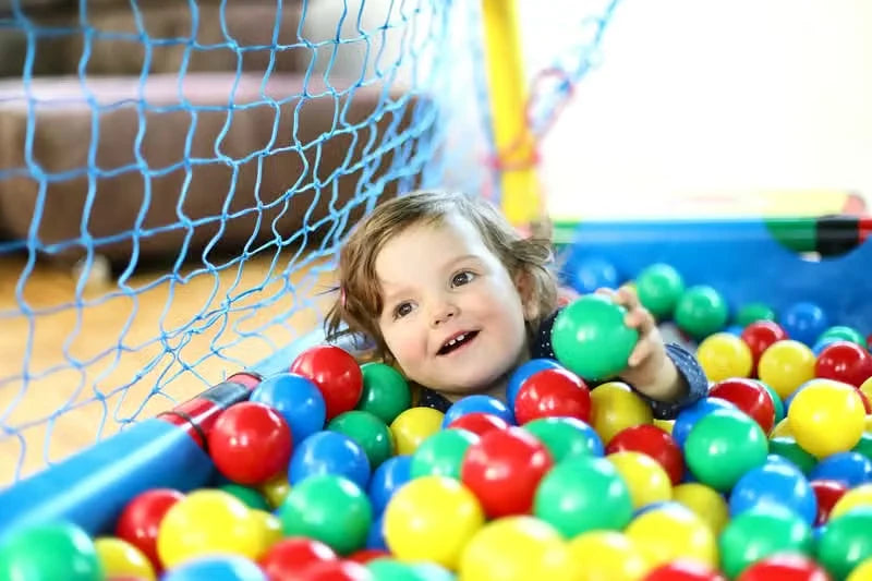 Child lying among colourful balls inside a netted QUADRO baby ball cage