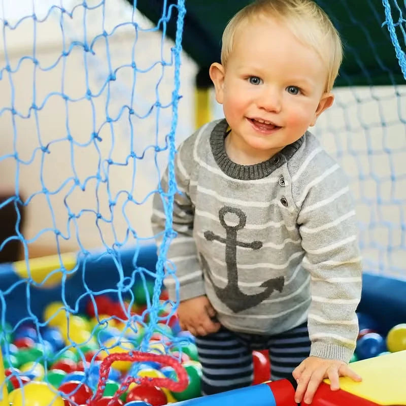 Toddler standing at the net opening of a QUADRO baby ball cage