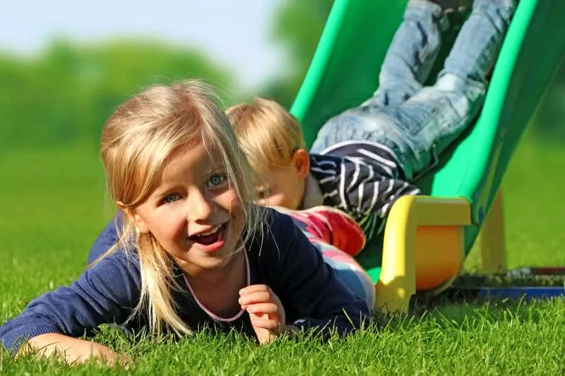 Two children lying on grass after using a green curved QUADRO slide