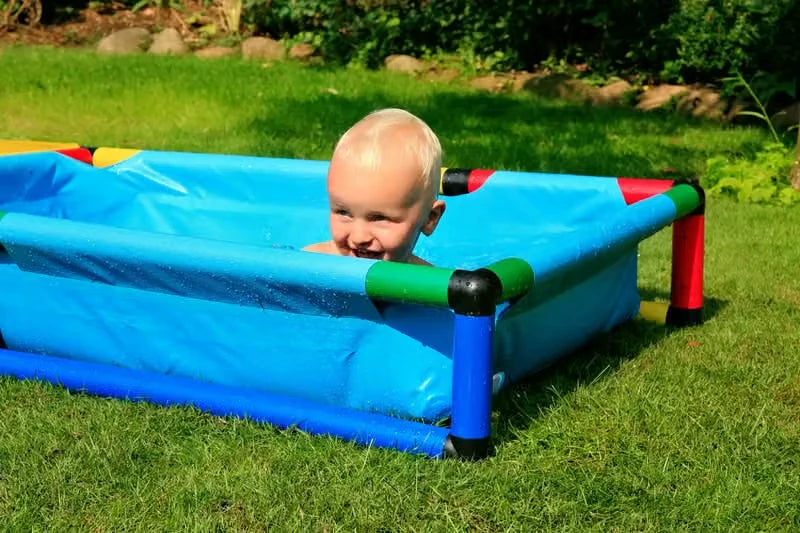Baby peeking over the blue liner of a small QUADRO pool on grass