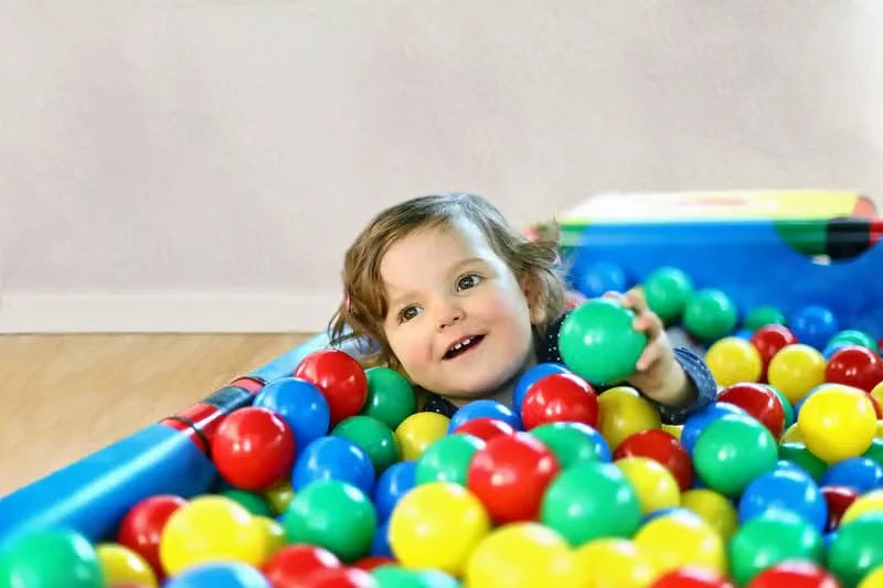 Child lying among colourful balls inside a small QUADRO pool