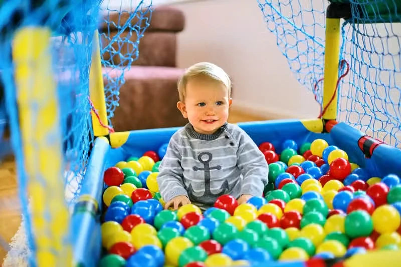 Smiling toddler seated in a small netted QUADRO ball pool