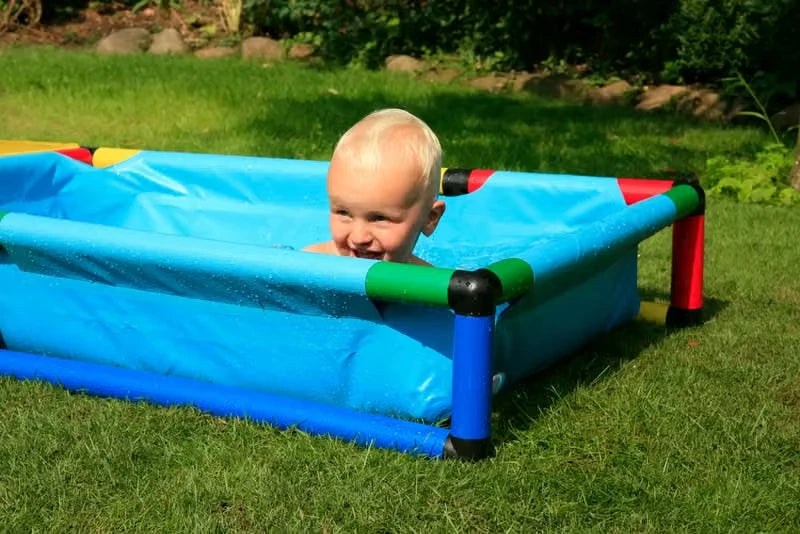 Baby peeking over the side of a small blue QUADRO pool outdoors